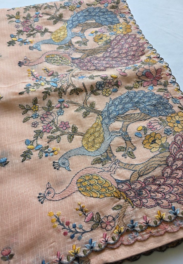 Hand embroidered peacocks and pink flowers on the pallu of a pastel peach Kota saree